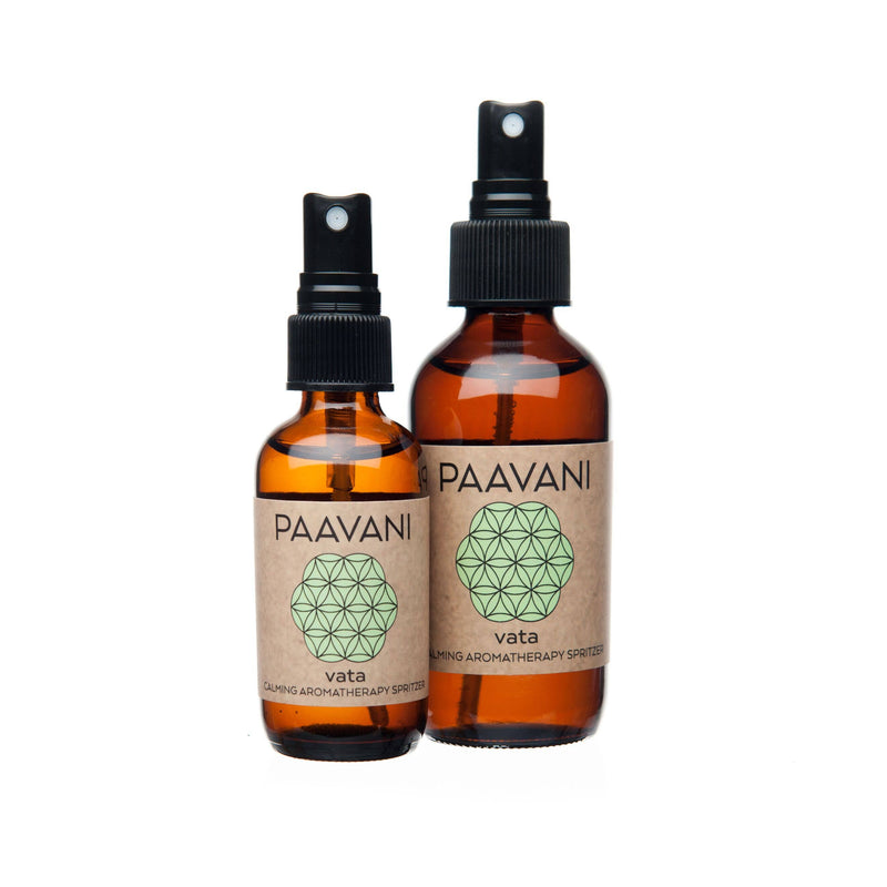 Zwei bernsteinfarbene Glasflaschen mit schwarzen Sprühköpfen, beschriftet mit "PAAVANI vata CALMING AROMATHERAPY SPRITZER", stehen nebeneinander vor weißem Hintergrund. Die Flaschen haben unterschiedliche Größen und beide zeigen ein hellgrünes geometrisches Muster auf ihren Etiketten.