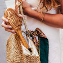 Frau nimmt eine Holzhaarbürste von Aumyana aus einer geflochtenen Strohtasche.