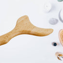 Nahaufnahme eines geschwungenen hölzernen Massagegeräts auf weißem Hintergrund mit unscharfen Wellness-Artikeln.