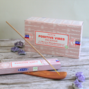 SATYA „Positive Vibes“ Räucherstäbchen-Display-Box und Einzelpackung auf einem Holzhintergrund, mit einem Stäbchen in einem Halter und Amethystkristallen.