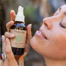 Eine Frau hält eine Flasche Paavani Ayurveda Vata Toner für trockene Haut und sprüht es sich gleich auf ihr Gesicht.