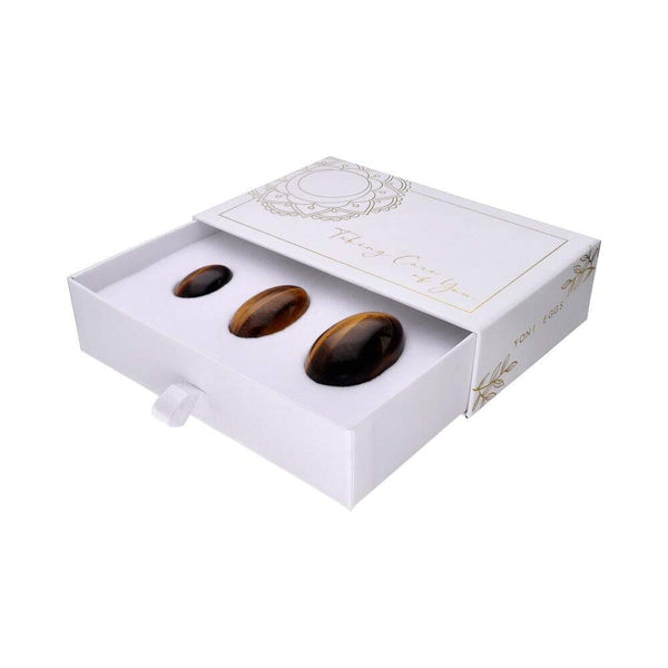 Geöffnete weiße Schachtel mit einem Set von drei polierten, braunen Tigerauge Yoni-Eiern in aufsteigenden Größen.