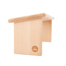 Schrägansicht der hellen Buchenholz-Meditationsbank mit abgerundetem Sitzflächenrand und massiven Beinen, Logo-Gravur am vorderen Bein sichtbar, auf weißem Hintergrund.