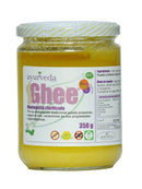 Ein Glasgefäß mit "Ayurveda autentico Ghee" (geklärte Butter) mit gelb-weiß gestreiftem Deckel. Das violette Vorderetikett trägt die Aufschrift "Mantequilla clarificada", mit Symbolen für "BIO", "100% Natural", "Sin Gluten", "OMG" (gentechnikfrei) und "350 g".