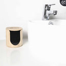 Ein Bambushalter mit schwarzen wiederverwendbaren Make-up-Entfernerpads, auf einer weißen Waschbeckenplatte unter einem Wasserhahn platziert.