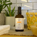 Eine bernsteinfarbene Pumpspender-Flasche Gesichtsmassageöl für fettige Haut auf einer Theke mit Pflanzen und Handtüchern.