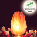 Eine hell leuchtende, handgefertigte Himalaya-Salzlampe steht inmitten von rosa und weißen Rosen sowie kleinen brennenden Kerzen in einer dunklen Umgebung.