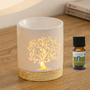 Eine beleuchtete, weiße Keramik-Duftlampe mit leuchtendem Lebensbaum-Ausschnitt, die neben einer Flasche Zen'Arôme „Douce Nuit Synergie“ ätherisches Öl steht.