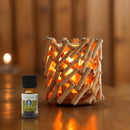 Flasche des ätherischen Öls Zen'Arôme Douce Nuit Synergie neben einem rustikalen Kerzenhalter aus Holz, in dem ein warmes Licht leuchtet.