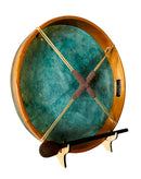 Eine runde Rahmentrommel (Schamanentrommel) mit hellem Holzrand und einem einzigartig bemalten Fell in gesprenkelten Petrol-/Kupferpatina-Tönen, die die gekreuzte braune Schnürung auf der Rückseite zeigt und auf einem Holzständer ruht, mit einem dunklen Schlägel davor.