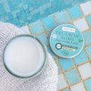 Offener Tiegel Aumyana Gel-Crème Aloha auf blauen Poolfliesen und einem weißen Handtuch.