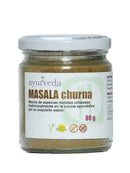 Glas Masala Churna mit weißem Deckel. Das weiße Etikett zeigt "Ayurveda Masala Churna", die Füllmenge von 80g und den Hinweis "Mezcla de especias molidas utilizadas tradicionalmente en la cocina ayurvédica".