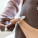 Nahaufnahme einer Person, die eine kleine Avani Ayurveda Roll-on-Flasche mit Öl in der Nähe ihres Bauches hält.