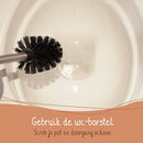 Eine Toilettenschüssel wird mit einer Toilettenbürste gereinigt, mit niederländischem Text "Gebruik de wc-borstel Scrob je pot en doorgang schoon" (Benutze die WC-Bürste. Schrubbe dein Becken und den Abfluss sauber).