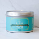 Eine metallische, zylindrische Dose Cacao Laboratory Ceremonial Grade Cacao in der Sorte „WATER“ (100% Kakao mit Koriander und Maca). Das Etikett ist ein beruhigendes Hellblau mit goldenen Akzenten und zeigt das Nettogewicht von 8oz (226.8g).
