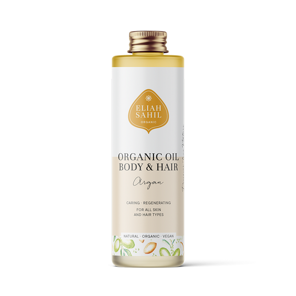 Produktfoto einer hohen weißen Flasche „Eliah Sahil Organic Oil Body & Hair Argan“ mit einem hellbraunen Etikett und goldenem Logo, das besagt, dass es pflegend und regenerierend für alle Haut- und Haartypen ist.