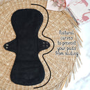 Schwarze wiederverwendbare Binde auf einer geflochtenen Matte, ihre natürlichen Kurven zur Rutschsicherung hervorgehoben, neben einem floralen Stoff.