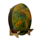 Eine runde Handtrommel (Rahmen- oder Schamanentrommel) mit einem bemalten Fell in gesprenkelten Gelb-, Orange- und Grüntönen, die aufrecht auf einem kleinen Holzständer ruht, mit einem hölzernen Schlägel davor platziert.