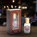 Eine kleine Glasflasche des Song of India "Wild Rose" Attar (natürliches Duftöl) neben der dekorativen, gemusterten Verpackung, auf einer Holzoberfläche mit verschwommenem Hintergrund.