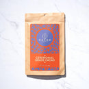 Ein Standbodenbeutel Cacao Laboratory Ceremonial Grade Cacao (Nettogewicht 1lb/453g) auf einer weißen Marmoroberfläche. Das Etikett hat ein auffälliges orange-lila Design mit einem zentralen Kakao-Logo.