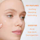 : Nahaufnahme einer Frau, die ein flüssiges Hautpflegeprodukt auf ihr Gesicht aufträgt, begleitet von Text, der die Hauptmerkmale (beruhigend, reparierend, feuchtigkeitsspendend) und die Anwendungsbereiche (Akne, dunkle Flecken, geschädigte Haut) hervorhebt.