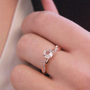 Nahaufnahme einer Hand mit einem roségoldenen Bypass-Verlobungsring mit rundem Diamanten.