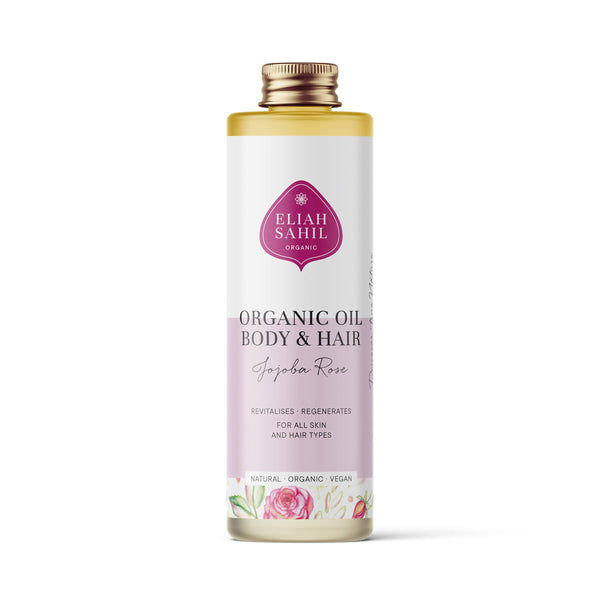 Produktfoto einer hohen weißen Flasche „Eliah Sahil Organic Oil Body & Hair Jojoba Rose“ mit einem hellrosa Etikett, das das Markenlogo und Rosenillustrationen zeigt.