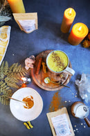 Eine Draufsicht auf eine goldene Latte-Tasse, Pulver, Gewürze, Kristalle und Kerzen auf einem dunklen Hintergrund.