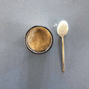 Aufnahme von oben auf ein Glas mit hellbraunem Pulver und einem Löffel mit einem kleinen Haufen Pulver daneben auf einer grauen Oberfläche.