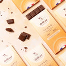 Eine Oberansicht von mehreren Delikao "Get up & Go" Milchschokoladenriegeln mit knisternder Füllung in ihren geöffneten Packungen, umgeben von zerbrochenen Schokoladenstücken, auf einem beigefarbenen Hintergrund.