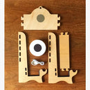 Ein zerlegter Ladeständer aus Holz mit drei lasergeschnittenen Holzteilen, einem runden magnetischen Ladegerät und einem USB-Kabel, auf einem Holztisch liegend.