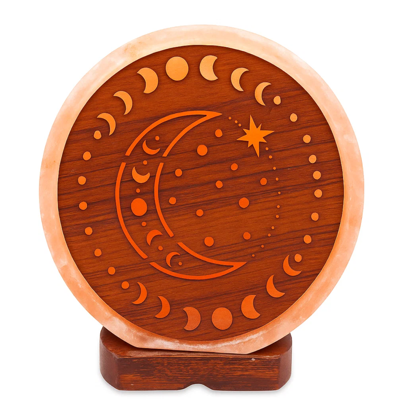Eine runde, geschnitzte Salzlampe mit einem Mondphasen-, Halbmond- und Stern-Design in einem Holzrahmen auf einem dunklen Holzsockel.