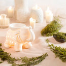 Ein keramischer Ölbrenner in Elefantenform, umgeben von Kerzen und grünem Laub.