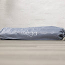 Eine hellgraue, zylindrische Yogamatten-Tasche mit Kordelzug und dem weißen „myoga“-Logo liegt horizontal auf einer Holzoberfläche vor einer strukturierten weißen Wand.