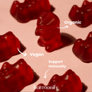 Mehrere rote Gummibärchen auf einer rosa Oberfläche, hervorhebend, dass die Harmonify-Gummis "Bio", "Vegan" und "Immununterstützend" sind.