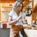 Eine Frau in einer Küche, die losen Tee aus einer Paavani-Ayurveda-Dose in eine Tasse löffelt.