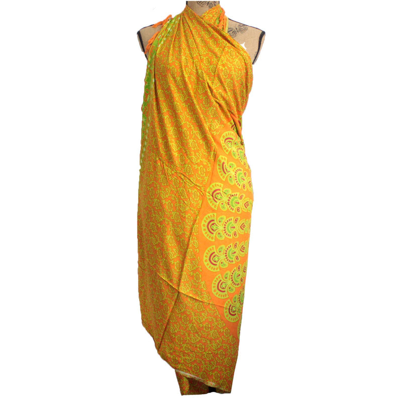 Ein orangefarbenes Sarong mit einem Pfauenmuster in Gelb und Grün, kunstvoll um eine Schaufensterpuppe drapiert, um als Strandtuch oder Überwurf zu dienen.