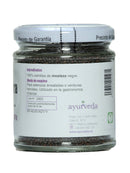 Das rückseitige Etikett eines Glasgefäßes mit "Ayurveda autentico Mostaza negra Semillas" (Schwarze Senfsamen). Es gibt die Inhaltsstoffe als 100 % schwarze Senfsamen an, mit Verwendungszwecken zum Würzen von Salaten oder gekochtem Gemüse und weist auf die Verwendung in der orientalischen Gastronomie hin.