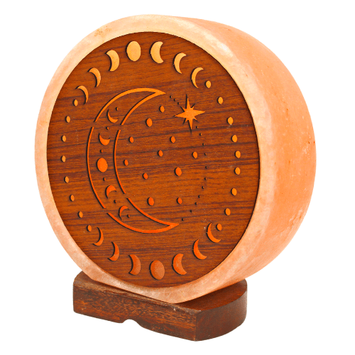 Eine runde, geschnitzte Salzlampe mit einem Mondphasen- und Stern-Design in einer Seitenansicht auf einem dunklen Holzsockel.