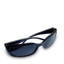 Eine schwarze Lochbrille (oder stenopäische Brille) liegt schräg und leicht geöffnet vor einem weißen Hintergrund. Die undurchsichtigen Gläser sind gleichmäßig mit kleinen, runden Perforationen für Sehtrainingsübungen bedeckt.
