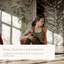 Eine Frau in einem Sport-BH führt in einem Studio mit unverputzten Ziegeln und Holzverkleidungen eine sitzende Yoga-Drehung aus. Das Bild enthält den italienischen Text: „Ossa, muscoli e articolazioni – Integratori a sostegno della muscolatura e delle osse".