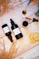 Eine Ansicht von oben von zwei schwarzen Flaschen und einer geöffneten Flasche Lion's Mane Flüssigextrakt mit einer Pipette, einem Löffel Flüssigkeit und Pilzpulver auf einem hellen Holzhintergrund.