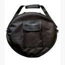 Eine runde, schwarze Nylontasche für ein Musikinstrument, wie eine Trommel oder Klangschale, mit einer kleinen Pattentasche, auf der „inner Rhythm“ aufgestickt ist, und einem Tragegurt.