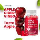 Eine Flasche Harmonify Apfelessig-Gummibärchen neben einem Stapel von drei roten Äpfeln, bewirbt den "Taste The Apple"-Geschmack und Produktvorteile wie Verdauungsunterstützung und Gewichtsmanagement.