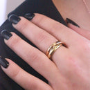 Ein goldener Trinity-Ring mit einem kleinen Diamanten an einer Hand mit schwarzen Fingernägeln.