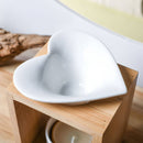 Eine Nahaufnahme, die die weiße, herzförmige Keramikschale einer Aromalampe aus Bambus mit einem darunter liegenden Teelicht zeigt.