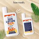 Zwei Flaschen Harmonify Sonnenlotion Kids LSF 50+, eine zeigt das Vorderetikett mit Breitband-Sonnenschutzdetails für empfindliche Haut, die andere das Rücketikett mit Gebrauchsanweisung und Inhaltsstoffen, auf sandigem Strandhintergrund mit Palmblättern.