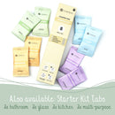 Eine Studioaufnahme (Flat-Lay), die eine hohe, hellgelbe Schachtel des COSMEAU Reinigungs-Tabs Starter Kit (8 Nachfüll-Tabs) und eine Ansammlung von acht einzelnen, farbigen Folien-Nachfüllpackungen drumherum zeigt: Küche Zitrone (hellgrün, 2x), Bad Orange (beige, 2x), Glas Blau (hellblau, 2x) und Mehrzweck Lavendel (lila, 2x). Der Text darunter wirbt für den Inhalt des Starter-Kits.