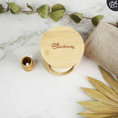 Ein Bambushalter, gefüllt mit weißen wiederverwendbaren Make-up-Entfernerpads, begleitet von einem kleinen Bambusbehälter für Wattestäbchen, auf einer weißen Marmoroberfläche mit einer grünen Pflanze im Hintergrund.