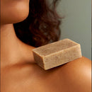 Ein Stück gesprenkelte braune Peelingseife liegt auf der Schulter einer Person.